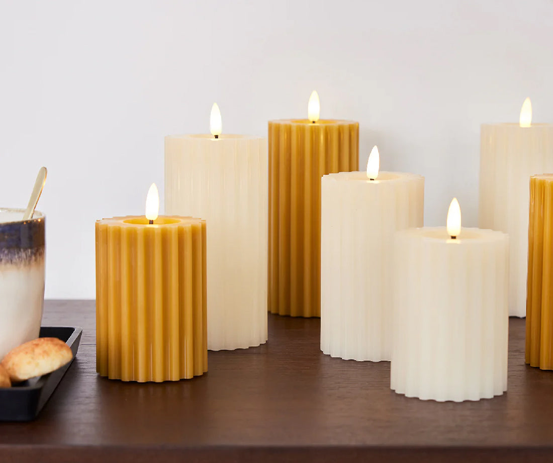 Weiße und senfgelbe LED-Kerzen stehen auf einem Holzregal.